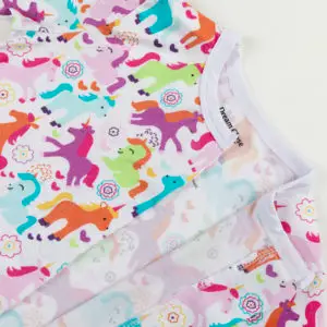 Haut de pyjama bébé décoré de licornes multicolores, fleurs, cœurs et étoiles sur fond blanc.