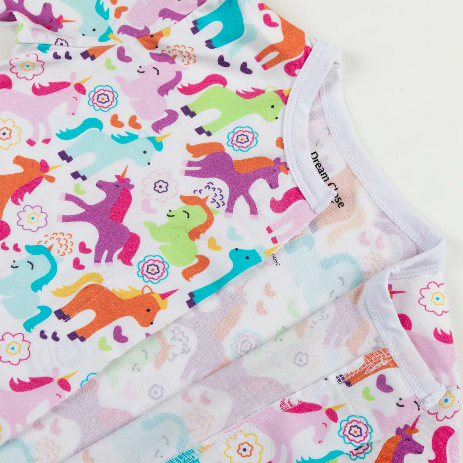 Haut de pyjama bébé décoré de licornes multicolores, fleurs, cœurs et étoiles sur fond blanc.