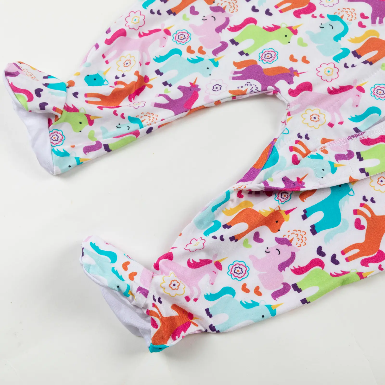 Bas de pyjama bébé décoré de licornes multicolores, fleurs et cœurs sur fond blanc.