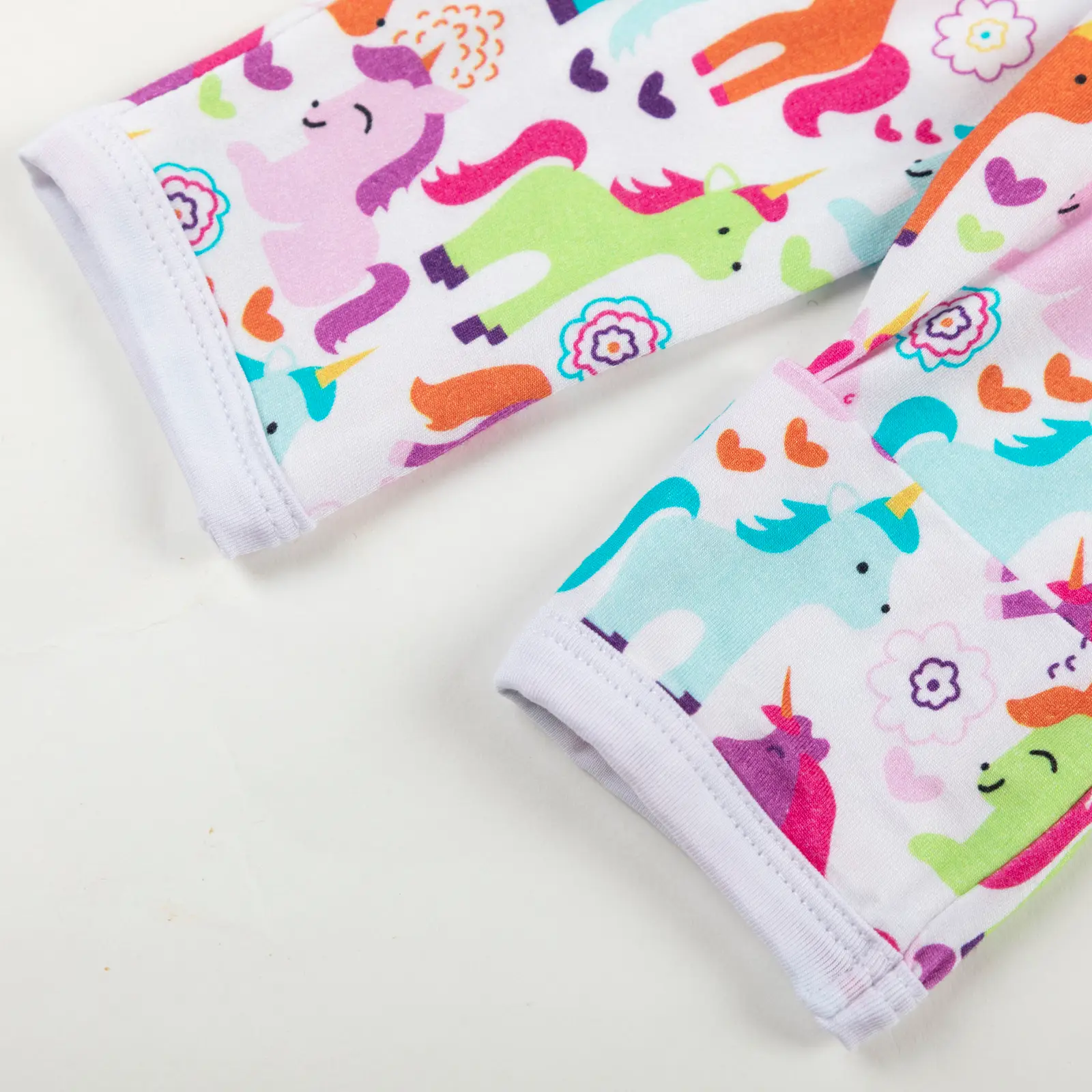 Manche rétractable de vêtement bébé décorée de licornes multicolores, cœurs et fleurs sur fond blanc.