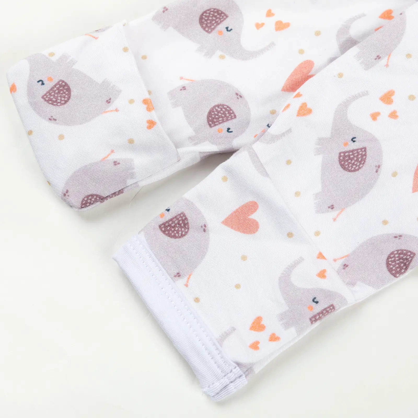 Manche rétractable de pyjama bébé décorée d’éléphants violets et de cœurs orange sur fond blanc.