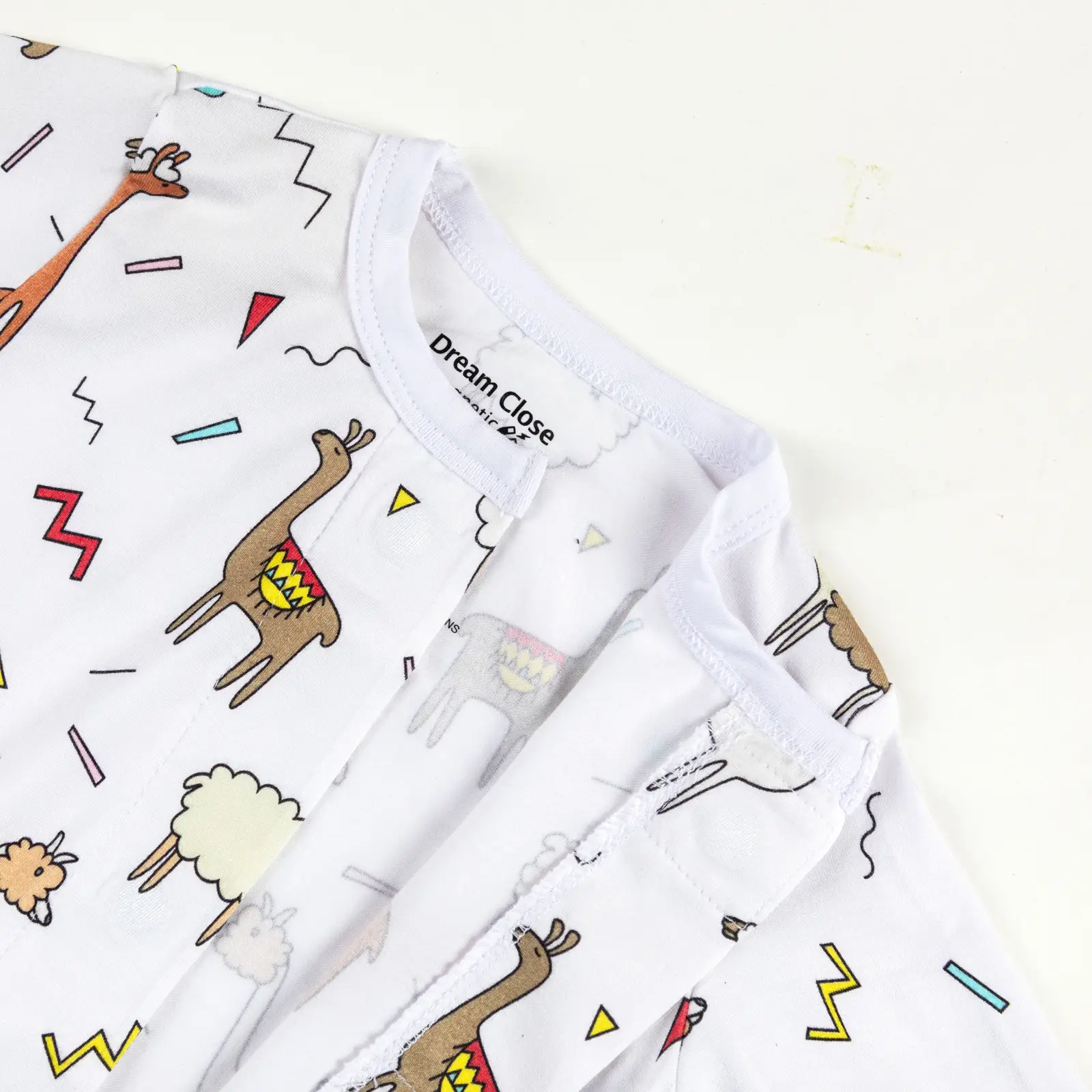 Haut de pyjama bébé décoré de lamas colorés et formes géométriques sur fond blanc.