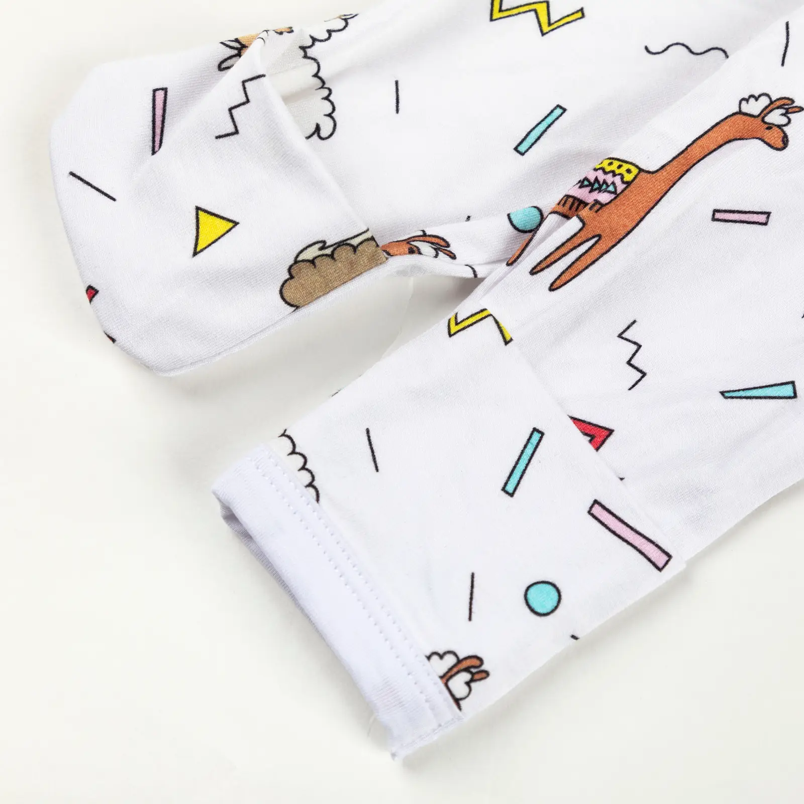 Manche rétractable de pyjama bébé décorée de lamas colorés et formes géométriques sur fond blanc.