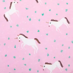 Motif imprimé licornes blanches sur fond rose pastel avec détails de brins d'herbe verts et pois blancs pour textile enfant.