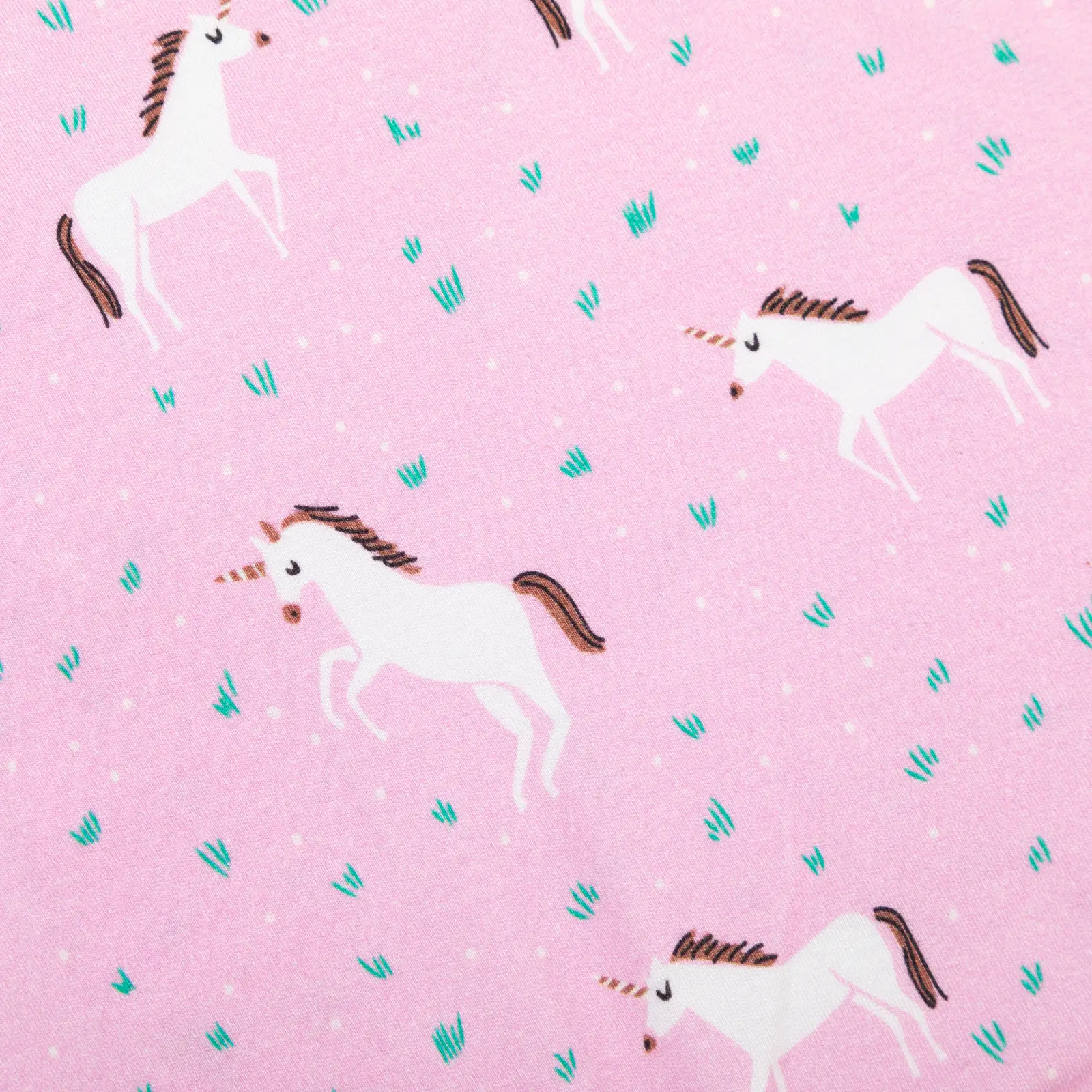 Motif imprimé licornes blanches sur fond rose pastel avec détails de brins d'herbe verts et pois blancs pour textile enfant.