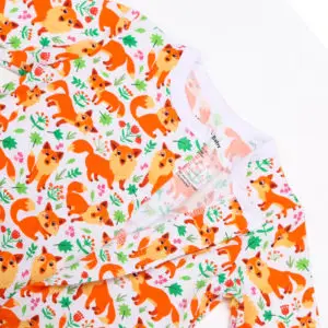 Haut de grenouillère bébé en tissu blanc décoré de renards orange, feuilles vertes et fleurs colorées dans un style ludique.