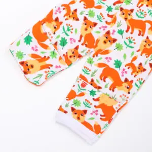 Manche de pyjama enfant en tissu blanc décorée de renards orange, feuilles vertes et fleurs colorées dans un style ludique.