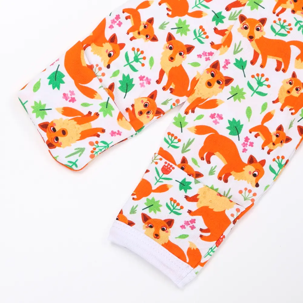 Manche de pyjama enfant en tissu blanc décorée de renards orange, feuilles vertes et fleurs colorées dans un style ludique.
