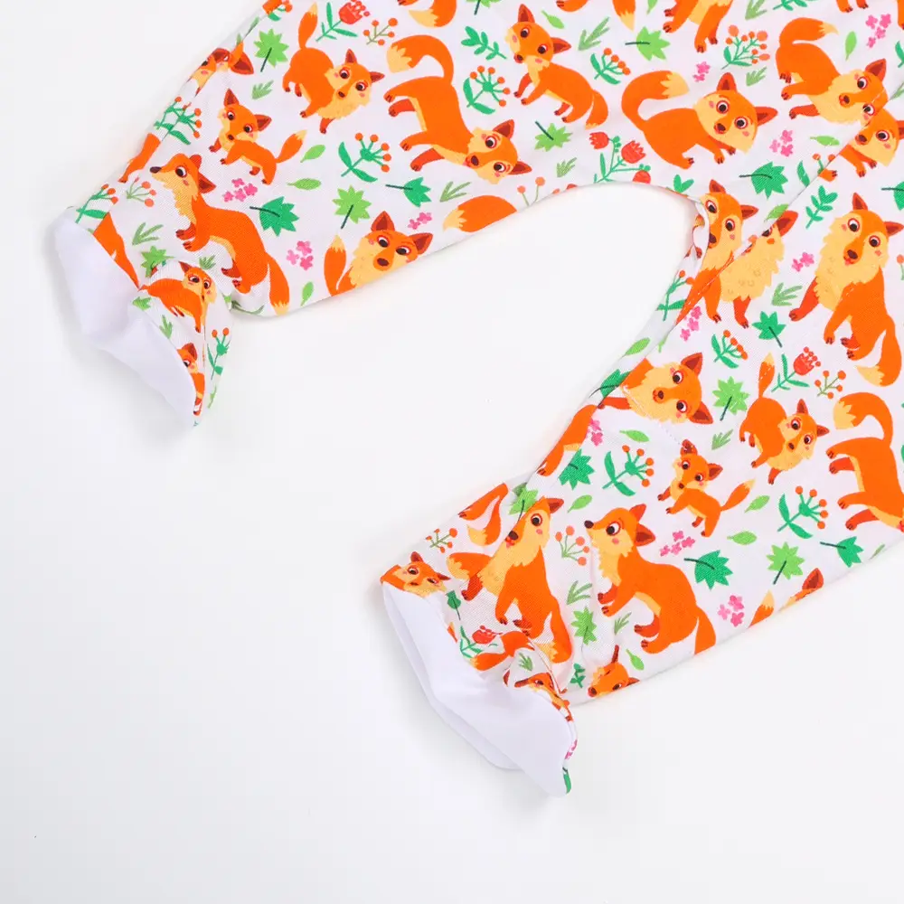 Pieds de pyjama enfant en tissu blanc décorés de renards orange, feuilles vertes et fleurs colorées dans un style ludique.